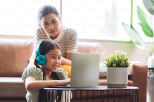Happiness asian family daughter study online from home with laptop while father mother is sitting together watch with cheerful smile ,asian child female wear headphone answer question from teacher