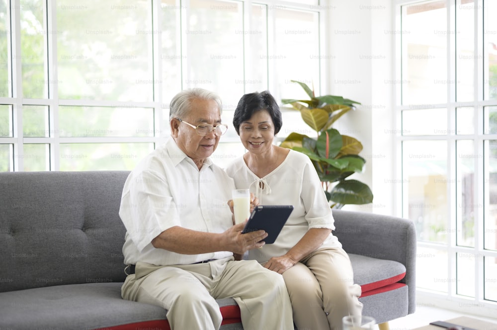 Ein glückliches älteres asiatisches Paar nutzt Tablet und spricht mit der Familie über die Webcam zu Hause, Ruhestandskonzept.