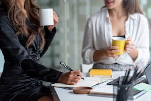 Happy two young Asian business woman holding coffee cup in office.