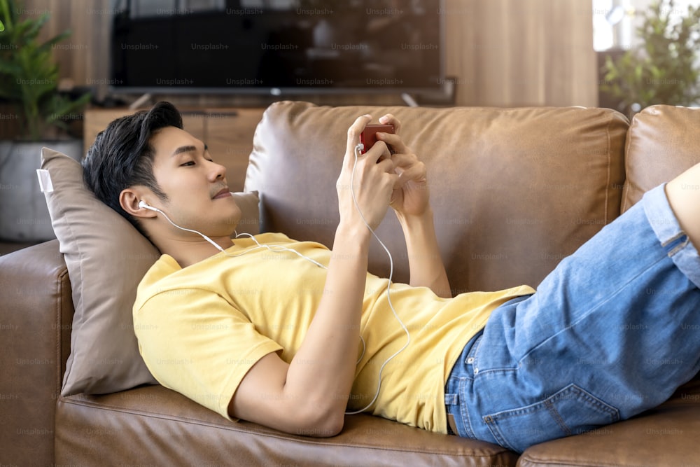 young asian male hand playing smartphone gaming online casual and leisure exiting and jpyful laydown on sofa on weekend at home quarantine activity ideas concept