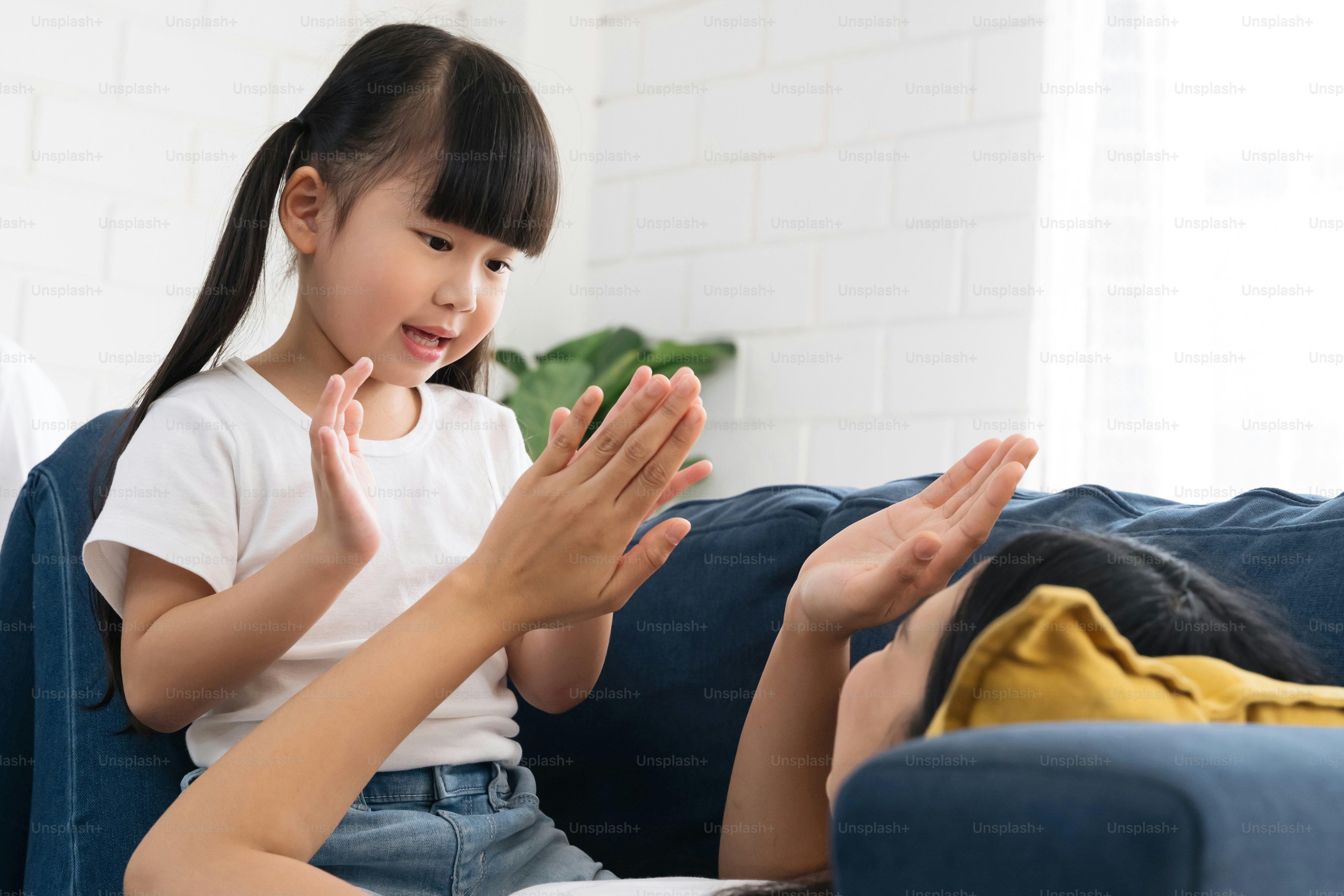 Asian cute girl enjoy playing with her mom on blue sofa. mother is playing wiith her daughter on sofa. Happy asian mom and daughter spending a good time togather.