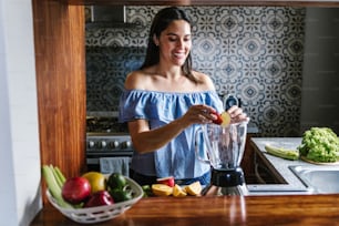 Latin Woman making green smoothie or Detox juice in kitchen at Home in healthy eating concept in Mexico