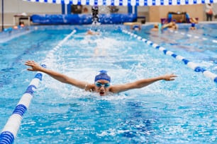 ラテンアメリカのプールでの水泳トレーニングで帽子とゴーグルを身に着けているラテン系の若い男のティーンエイジャーの水泳選手アスリート