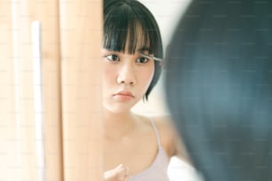 Concepto de quedarse en casa con estilo de vida de cuarentena. Mujer asiática adulta joven autocortada flequillo corte de pelo con tijeras. Ojos mirando a un espejo. Fondo en el día con la luz de la naturaleza.