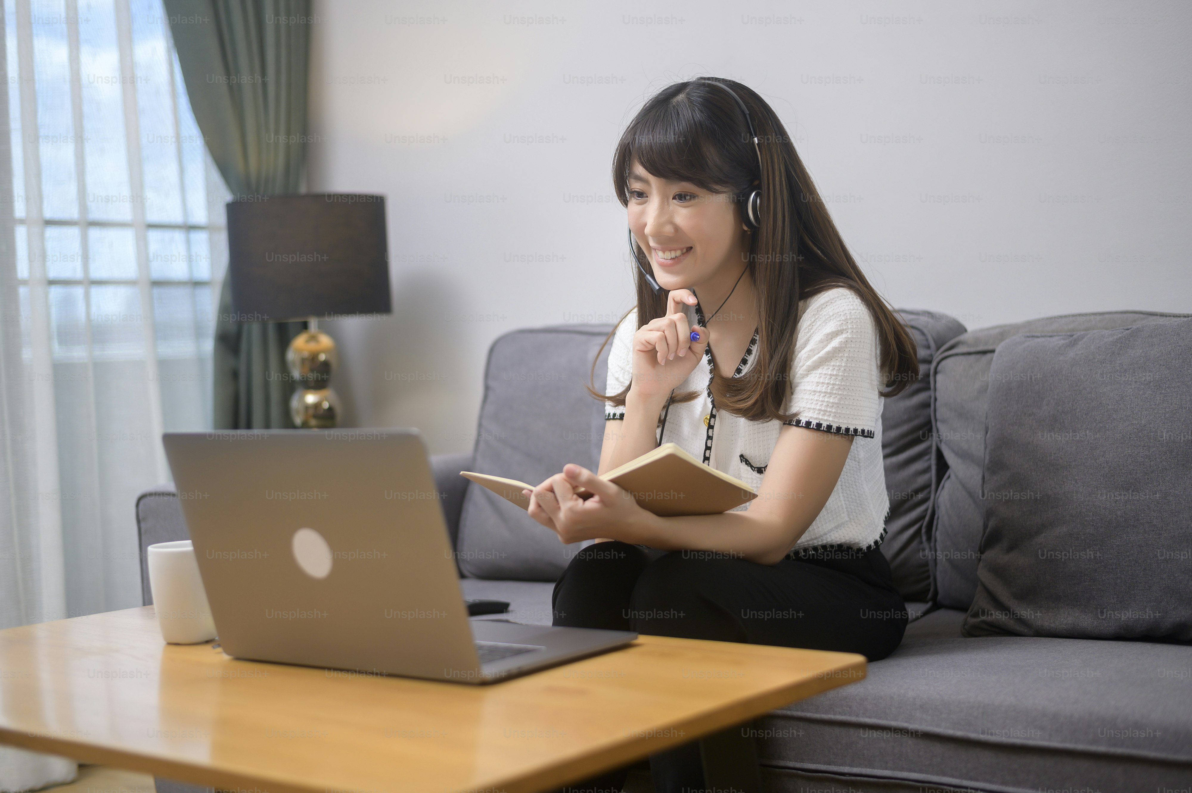 A beautiful young woman wearing headset is making video conference call via computer at home