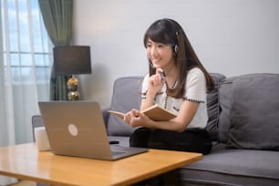 A beautiful young woman wearing headset is making video conference call via computer at home