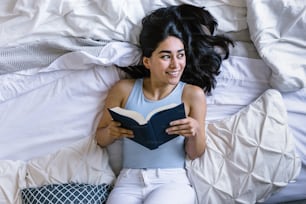 Young latin woman reading book and studying on bed at home in Mexico Latin America
