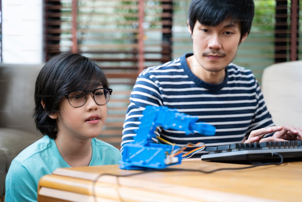 Asiatische Kinder programmieren Roboterkrane mit Laptops, um etwas über Technologie, Mathematik und Ingenieurwesen zu lernen. Programmieren und Programmieren zu Hause