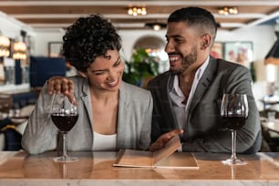 Young lovely couple enjoying at the bar in the evening. They are sitting at the bar with a glass of wine.