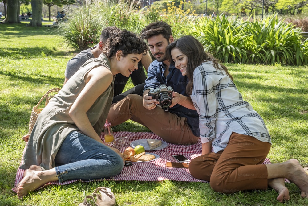 Friends at a picnic in a park. One of them is showing a picture he has just taken on his camera.