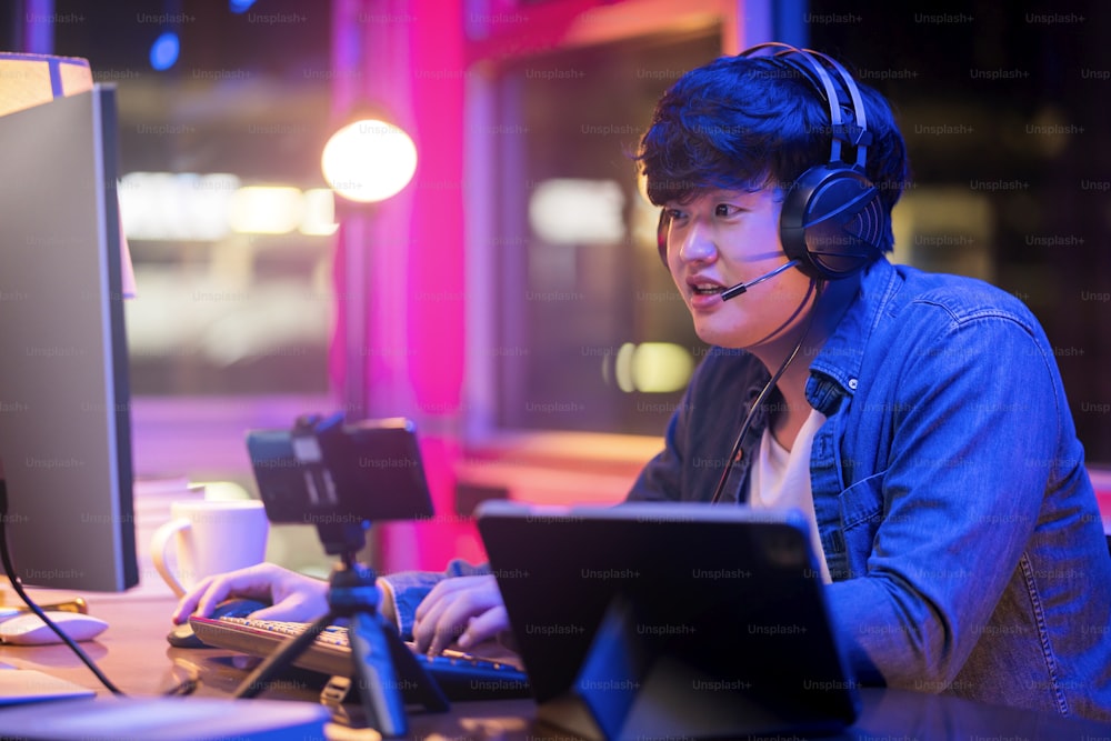 esport online game streaming asian male wear headset play dogital metaverse cyber space online match compettition sport game battle night time,young asia male enjoy exited gamer successful celebration