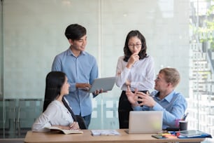 Grupo de jovens asiáticos modernos em roupas casuais inteligentes falando e sorrindo durante a reunião no escritório.