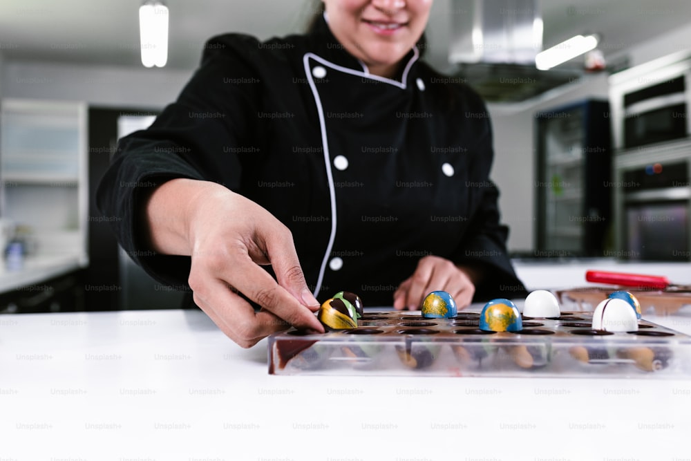mão de mulher latina chef confeiteiro vestindo uniforme preto no processo de preparação de deliciosos chocolates doces na cozinha no México América Latina
