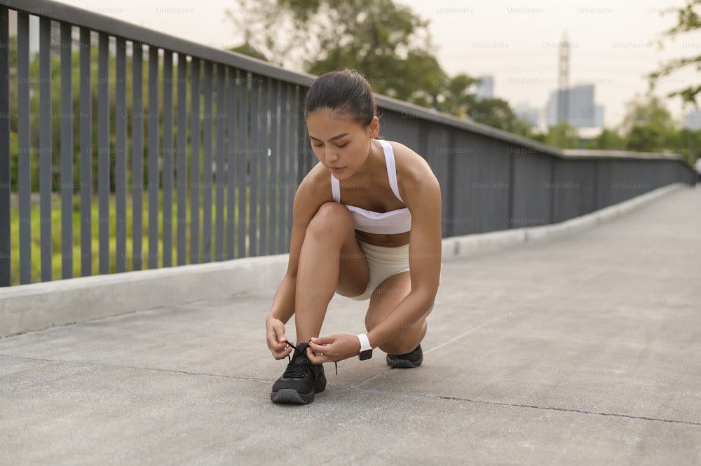 A young fitness woman in sportswear tying shoelace in city park, Healthy and Lifestyles.