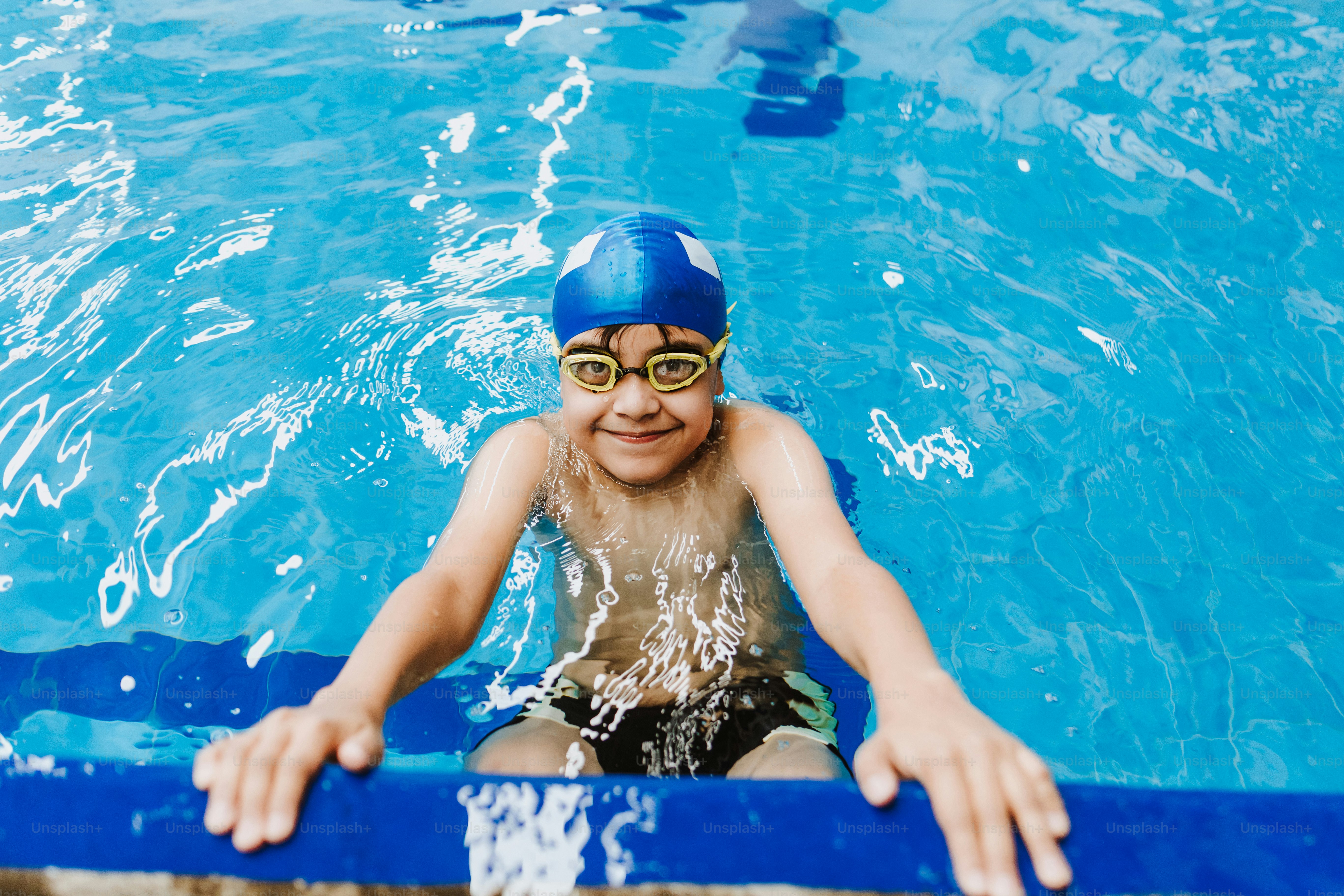 latin child boy swimmer wearing cap and goggles in a swimming training at the Pool in Mexico Latin America