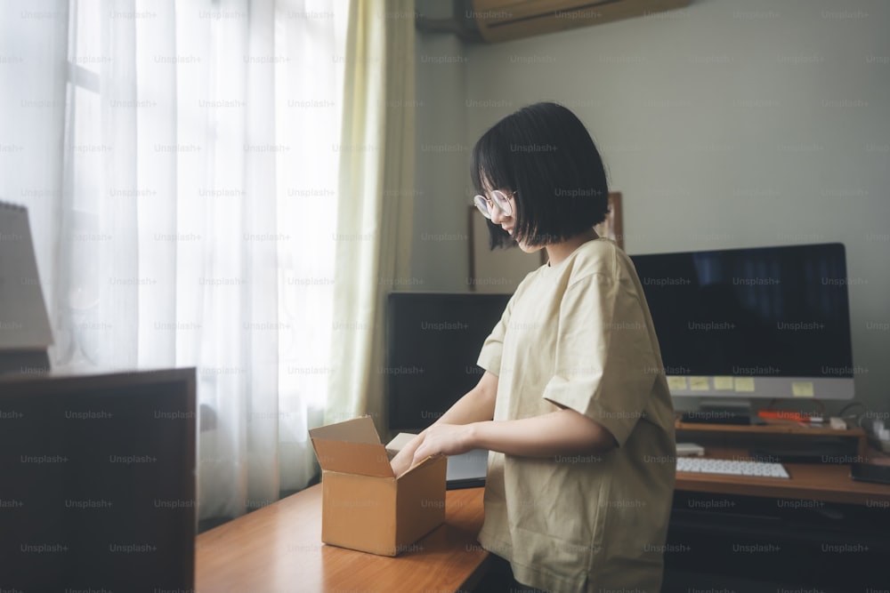 Young adult asian woman open box package. Deliverly from shopping application. Home office background with window days light. People buying order goods via online service concept.