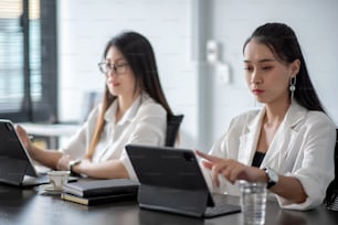 Dos jóvenes empresarias asiáticas son felices trabajando en presentaciones usando papeles y tabletas colocadas en la oficina.