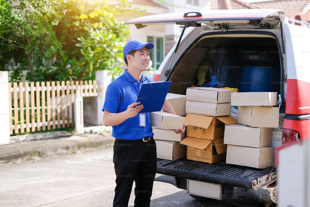 파란색 유니폼을 입은 젊은 배달원이 운송 차량으로 고객에게 보낼 제품 상자를 확인합니다.