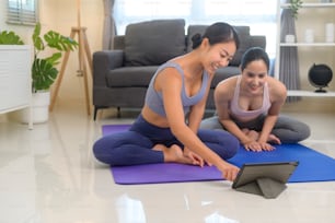 Fitte junge Freundinnen, die Yoga zu Hause über Online-Unterricht mit professionellem Lehrer, Sport und gesundem Lebensstilkonzept praktizieren.
