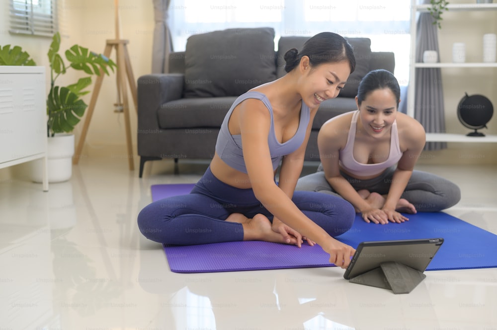 Fit young friend women practicing yoga at home via online class with professional instructor, sport and healthy lifestyle concept.