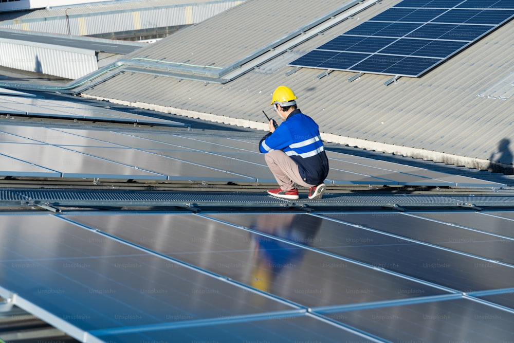 Asian technician installing inspection or repair solar cell panels on background field of photovoltaic solar panels solar cells on roof top factory.