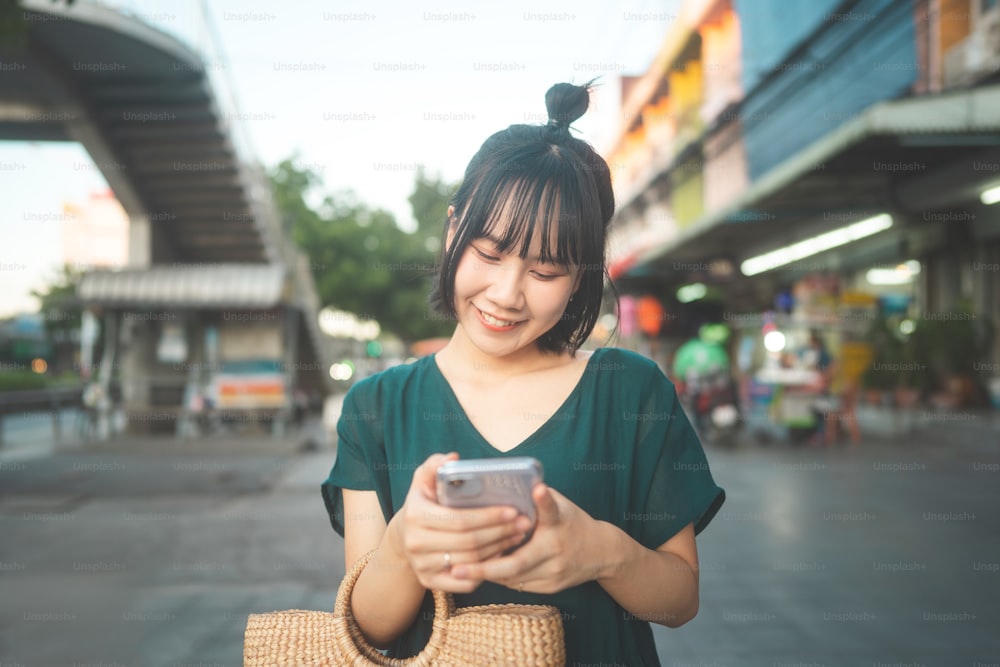 Happy smile young adult asian woman outdoor street market on evening. Using mobile phone for date application online. Casual look fashion lifestyle.