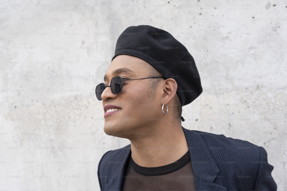 Young latin gay man with make-up on wearing a fashionable hat and sunglasses, isolated on a white background. LGBT.