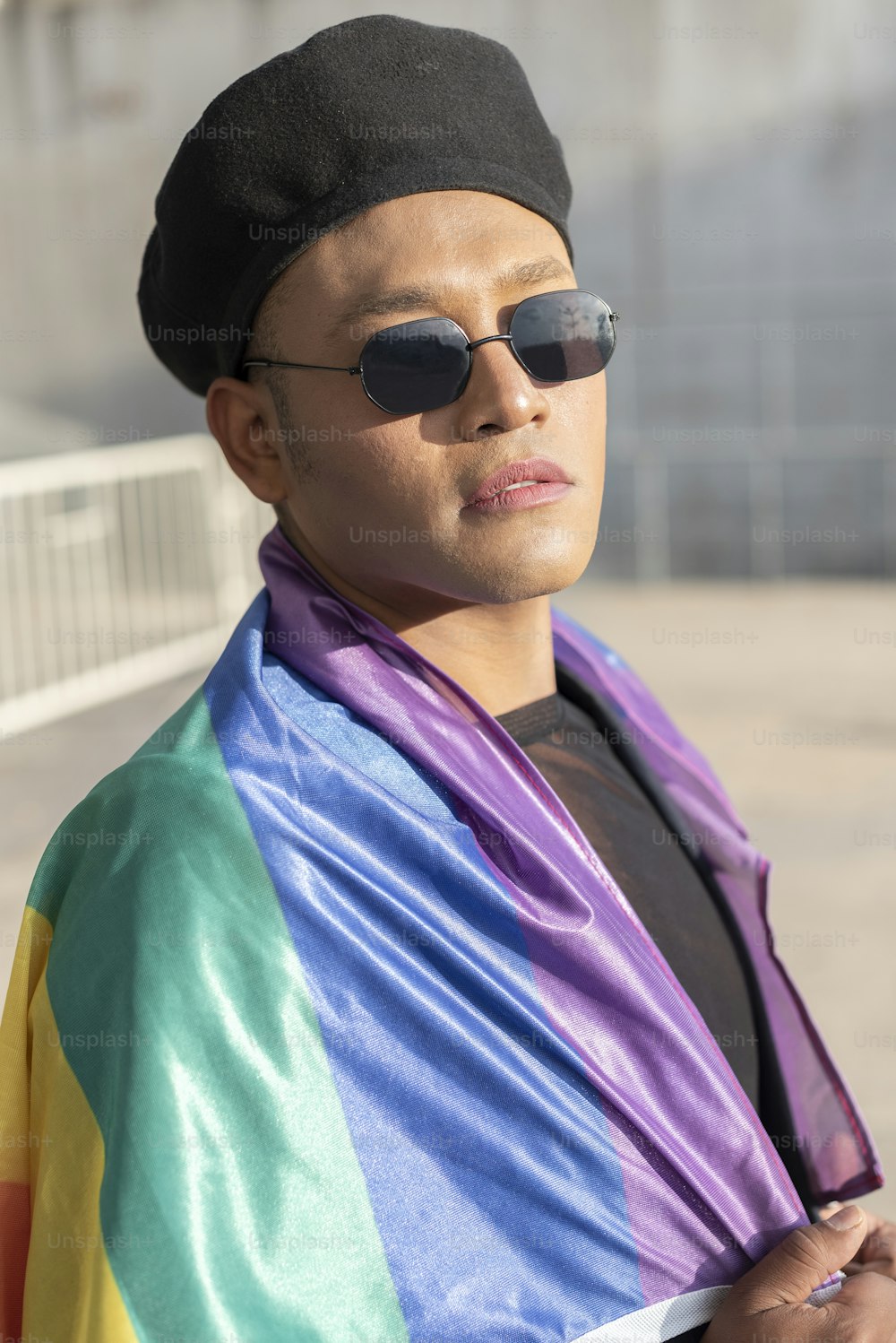 Hombre gay con maquillaje bajo la bandera del arco iris LGBT mientras mira a la cámara. Concepto de Orgullo. Mes del Orgullo.