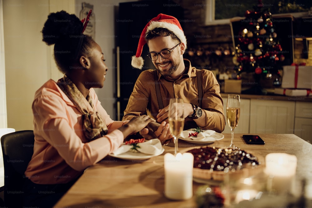 Happy couple enjoying in Christmas dinner and holding hands at dining table at home.