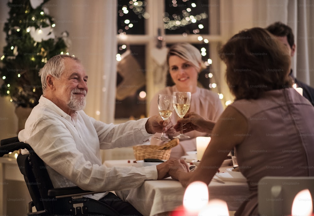 車椅子に乗った年配の男性と、屋内で一緒にクリスマスを祝い、グラスを鳴らしている。