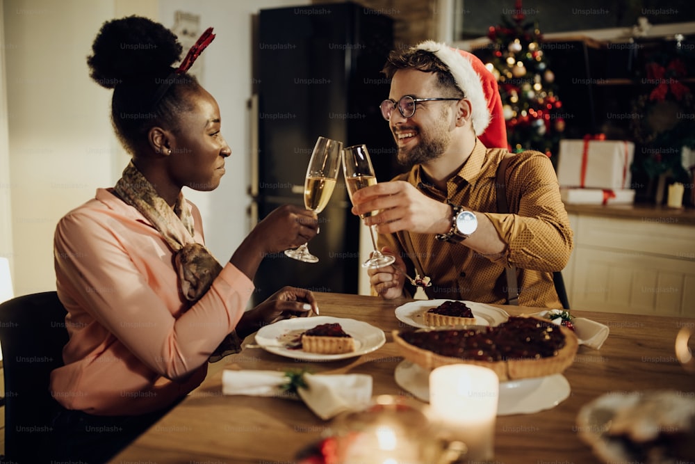 크리스마스 이브에 즐거운 시간을 보내고 식탁에서 샴페인으로 건배하는 젊은 행복한 커플.