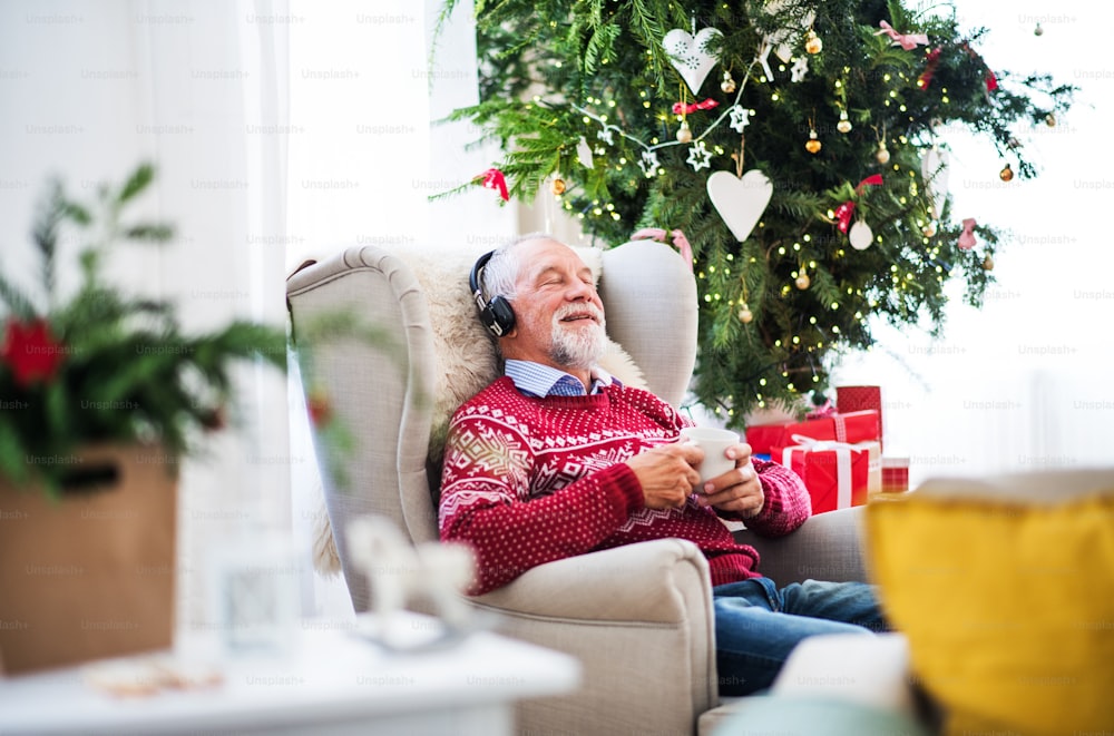 크리스마스 시간에 집에서 안락의자에 헤드폰을 끼고 앉아 음악을 듣고 하얀 컵을 들고 있는 노인의 초상화.