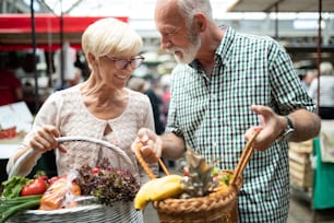 Smiling senior couple holding basket with vegetables at the grocery shop