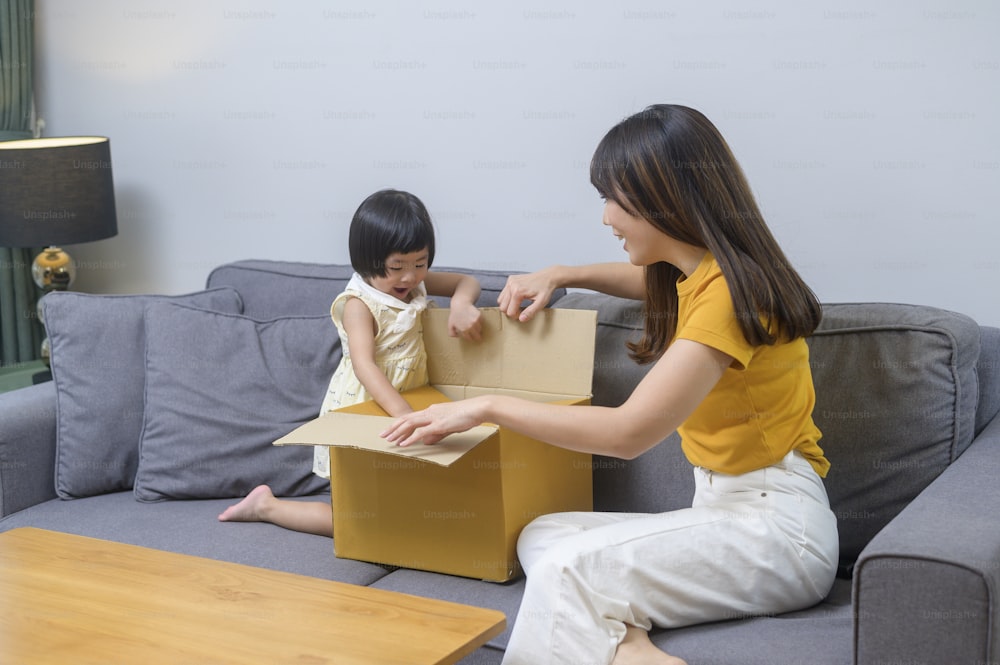 Una mamá feliz con una hija abriendo una caja de cartón en la sala de estar de casa