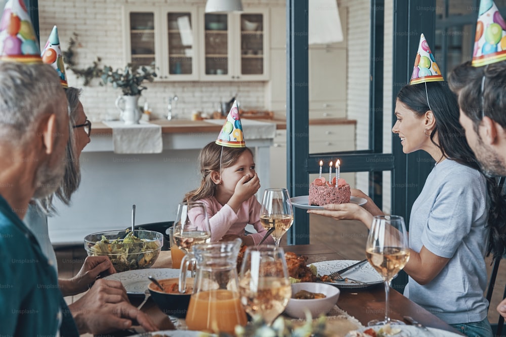 Happy family celebrating birthday of little girl while sitting at the dining table at home