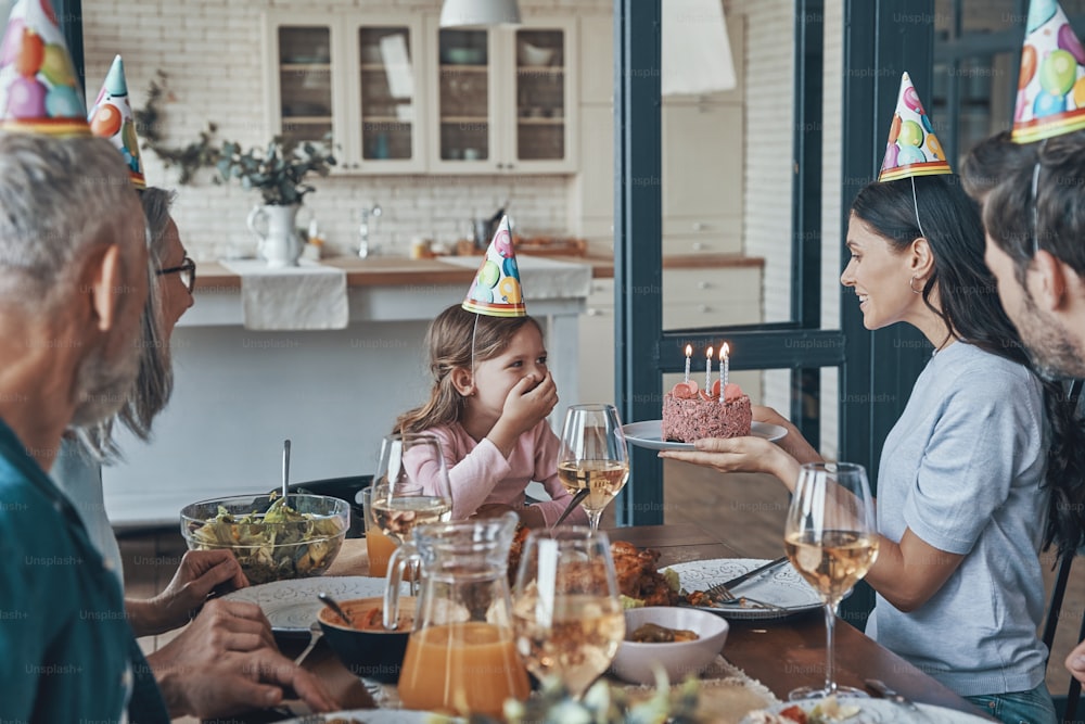 Glückliche Familie, die den Geburtstag eines kleinen Mädchens feiert, während sie zu Hause am Esstisch sitzt