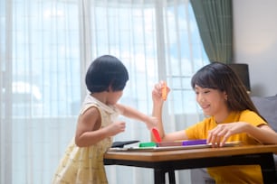 A young mom helping daughter drawing with colored pencils in living room at home.