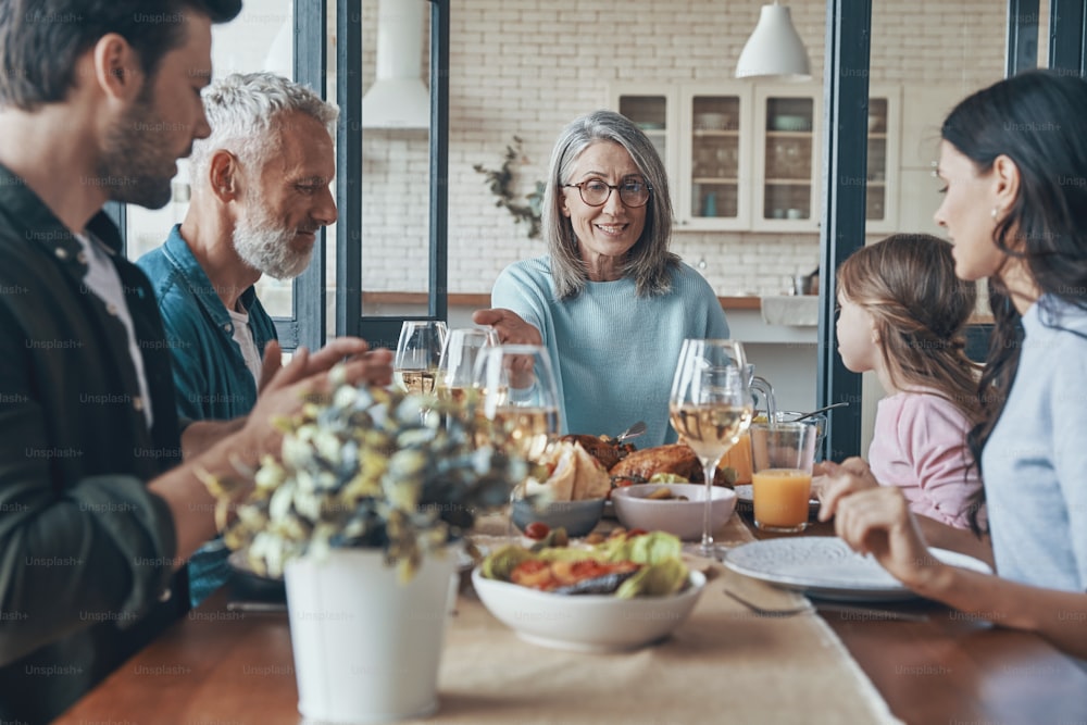 Familia multigeneracional feliz que se comunica y sonríe mientras cenan juntos