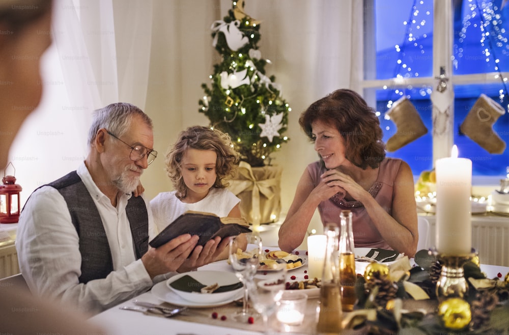 Kleines Mädchen mit Eltern und Großeltern drinnen, feiert Weihnachten und liest die Bibel.