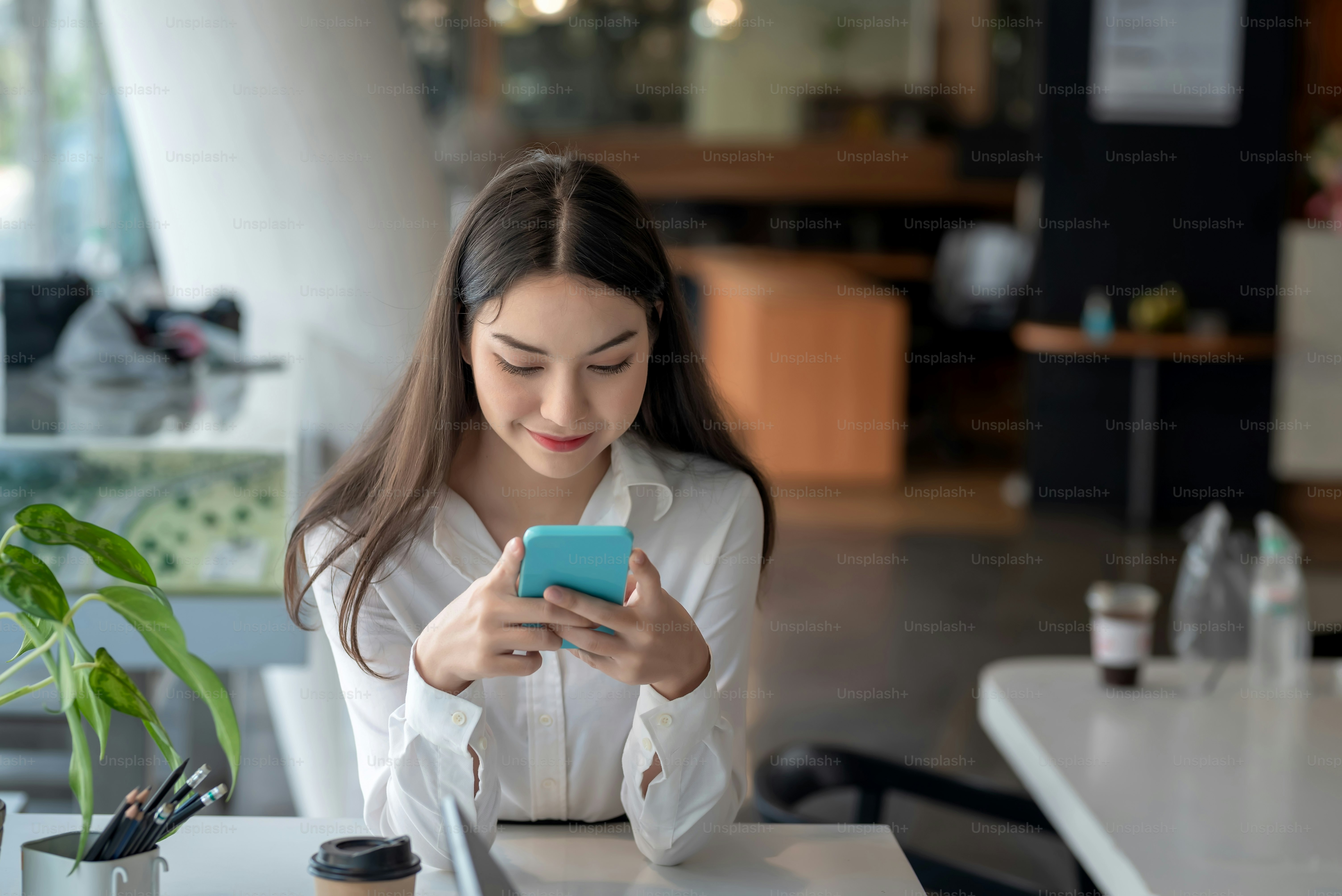 Wanita muda Asia senang bermain di ponsel di kantor.