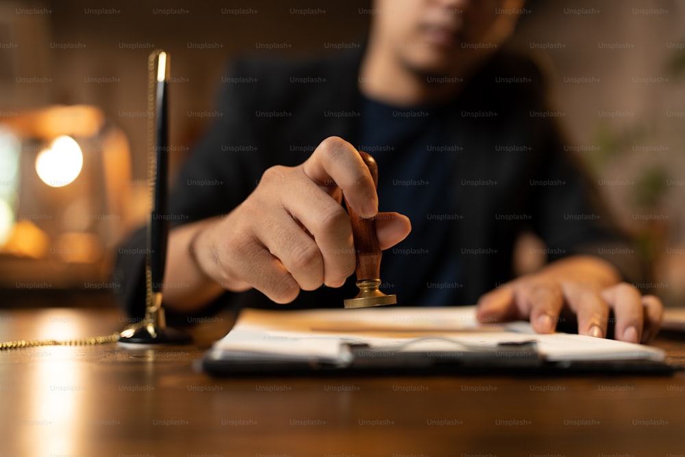 Close-up of a person's hand stamping with approved stamp on certificate document public paper at desk, notary or business people work from home, isolated for coronavirus COVID-19 protection