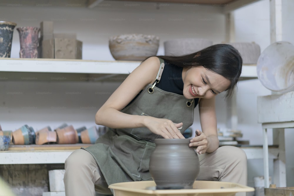 Primer plano de las manos femeninas que trabajan en la rueda de alfarero, mujer asiática de la escultura femenina que da forma al molde pequeño jarrón cuenco de arcilla en la rueda de alfarero en el estudio casero taller de arte y concepto de pasatiempo de creación