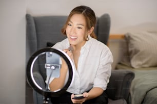Una hermosa bloguera de maquillaje asiática está transmitiendo en vivo cómo maquillarse la cara con belleza en su hogar, concepto de belleza y tecnología.