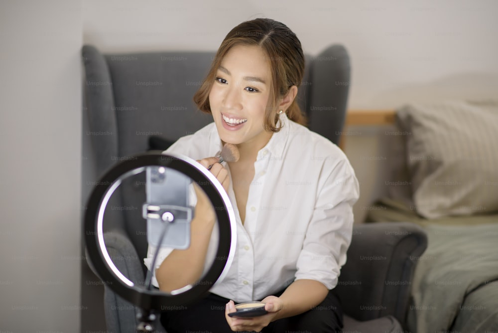 A beautiful Asian makeup blogger is live streaming how to beauty face makeup in her home, beauty and technology concept .
