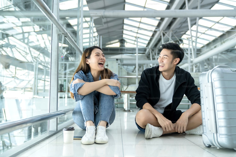 young asian casual cloths vacation travel couple friend sit relax laugh smile together on floor at public space safety travel new normal lifestyle waiting for time schedule for aboard departure