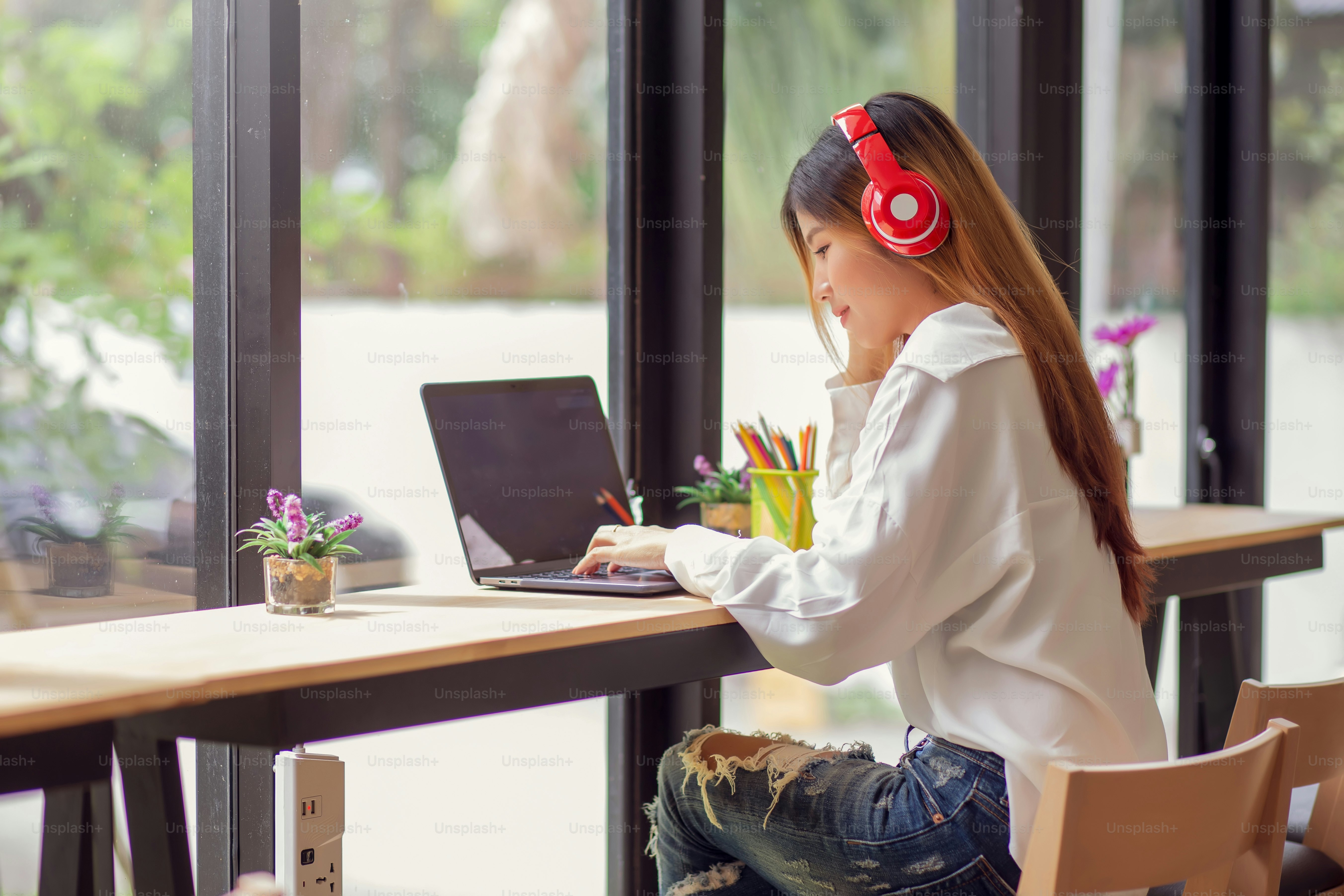 Potret wanita muda Asia mendengarkan musik dengan headphone dan menggunakan komputer laptop di kafe.