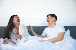 young Asian couple having pillow fight on bed in the morning, relaxing and happy at home