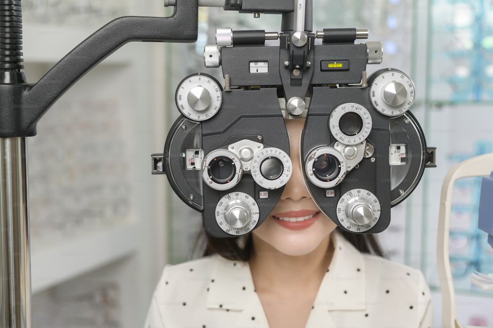 A Young female customer being examined visual test using Bifocal Optometry eyesight measurement device by ophthalmologist in optical center, eyecare concept.