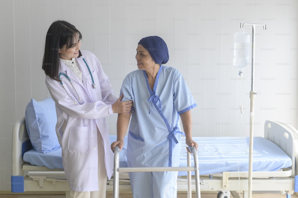 Doctor helping cancer patient woman wearing head scarf with walker at hospital, health care and medical concept