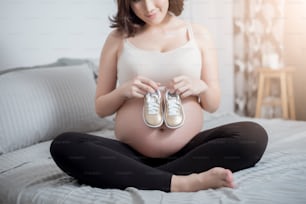 Hermosa mujer asiática embarazada que espera a su bebé con zapatos pequeños
